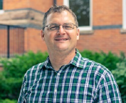 portrait of a smiling man with rectangular glasses and a flannel shirt