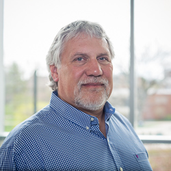 headshot of a man with short hair and beard, he is wearing a blue and white checkered button up