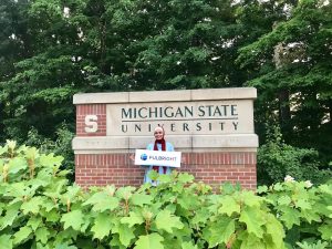 Student in front of MSU Sign holding Fulbright Sign