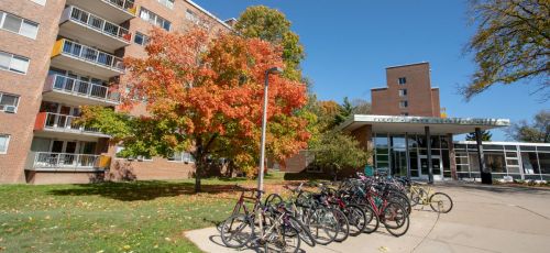 picture of a red brick dormitory with autumn colored trees and bikes at a bike rack